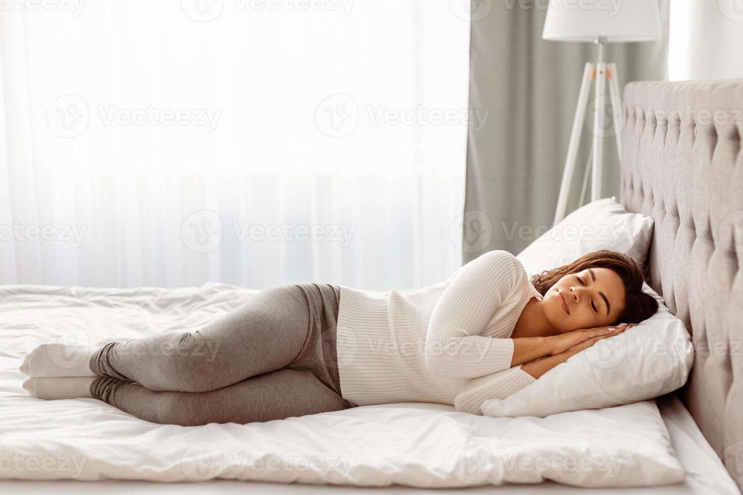 Full body length of calm young black woman sleeping well on the side. Beautiful African American lady resting, enjoying fresh cotton bedding, soft pillow and comfy mattress, banner, free copy space photo