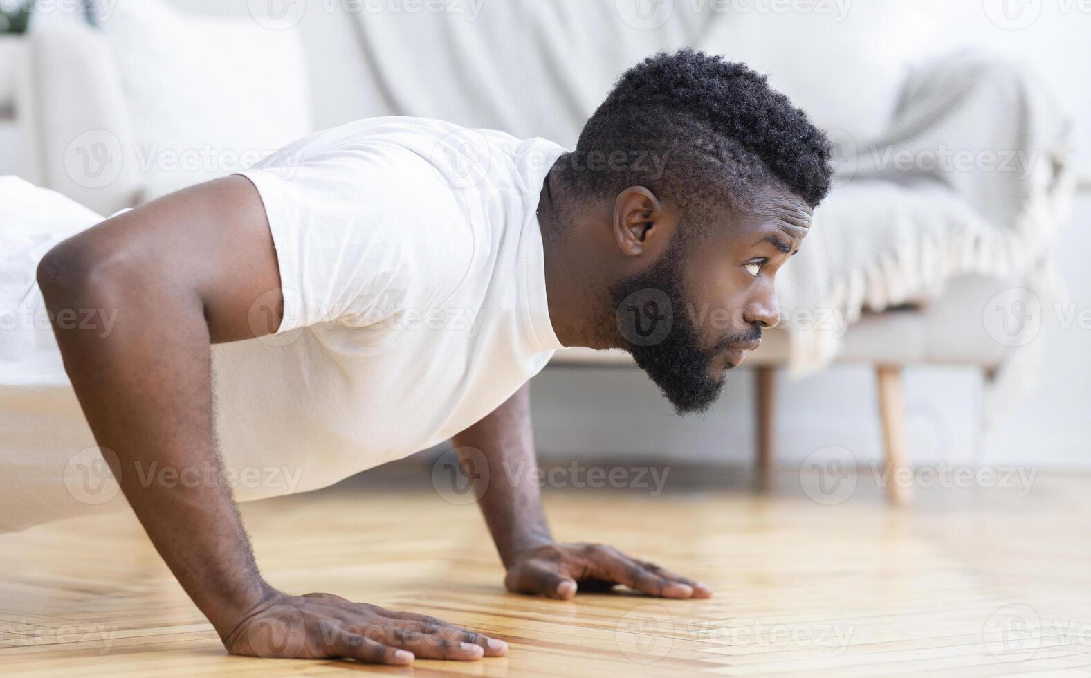 Young black man exercising in his house gym, doing push ups, side view, free space photo