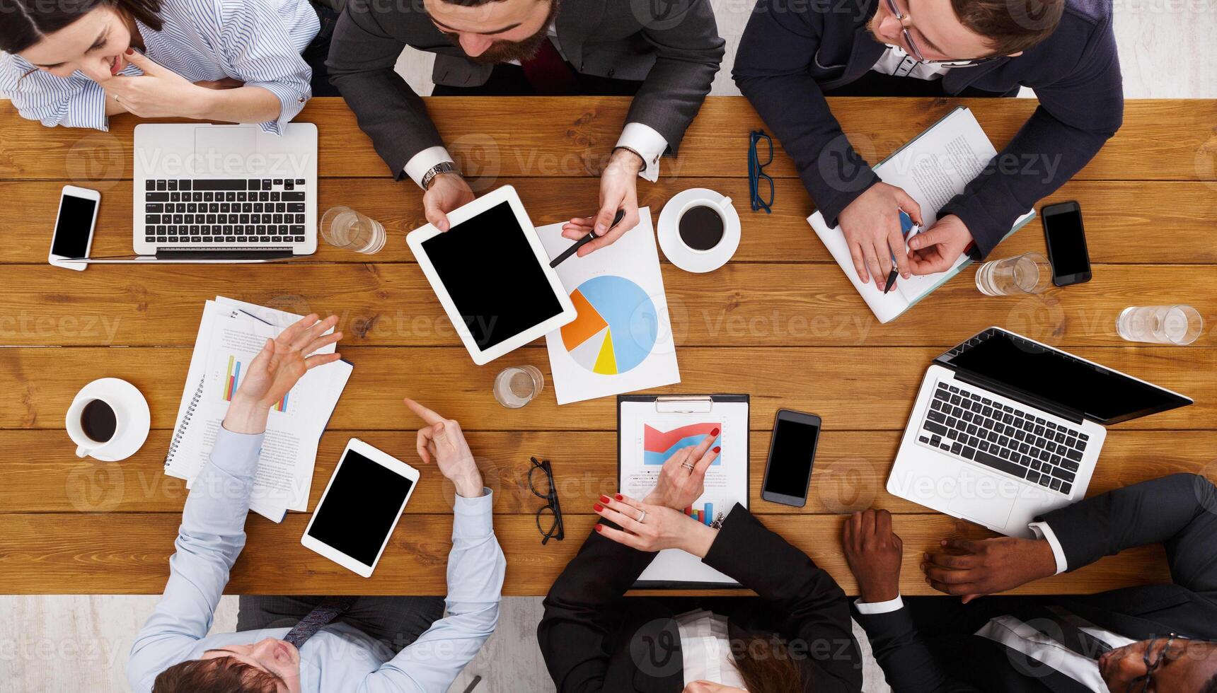Business meeting top view. Busy people work in office, above view of wooden table with mobile phones, laptop, tablet and documents papers with diagram. photo