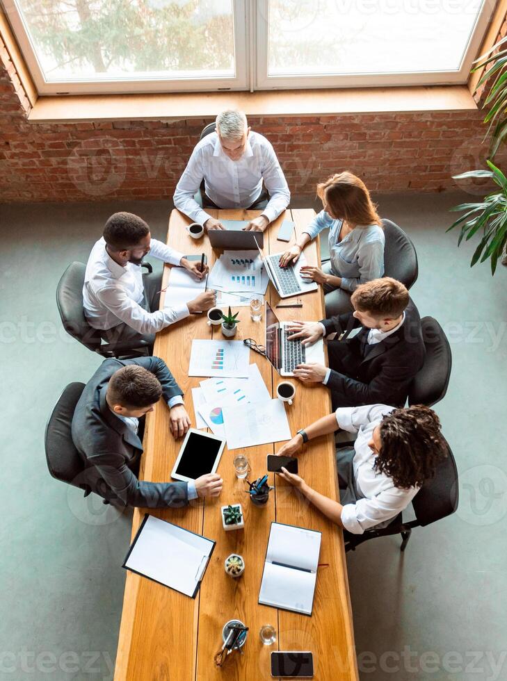 Teamwork. Diverse Coworkers Working Together Using Laptop And Tablet Computers Sitting At Desk In Modern Office. Above View photo