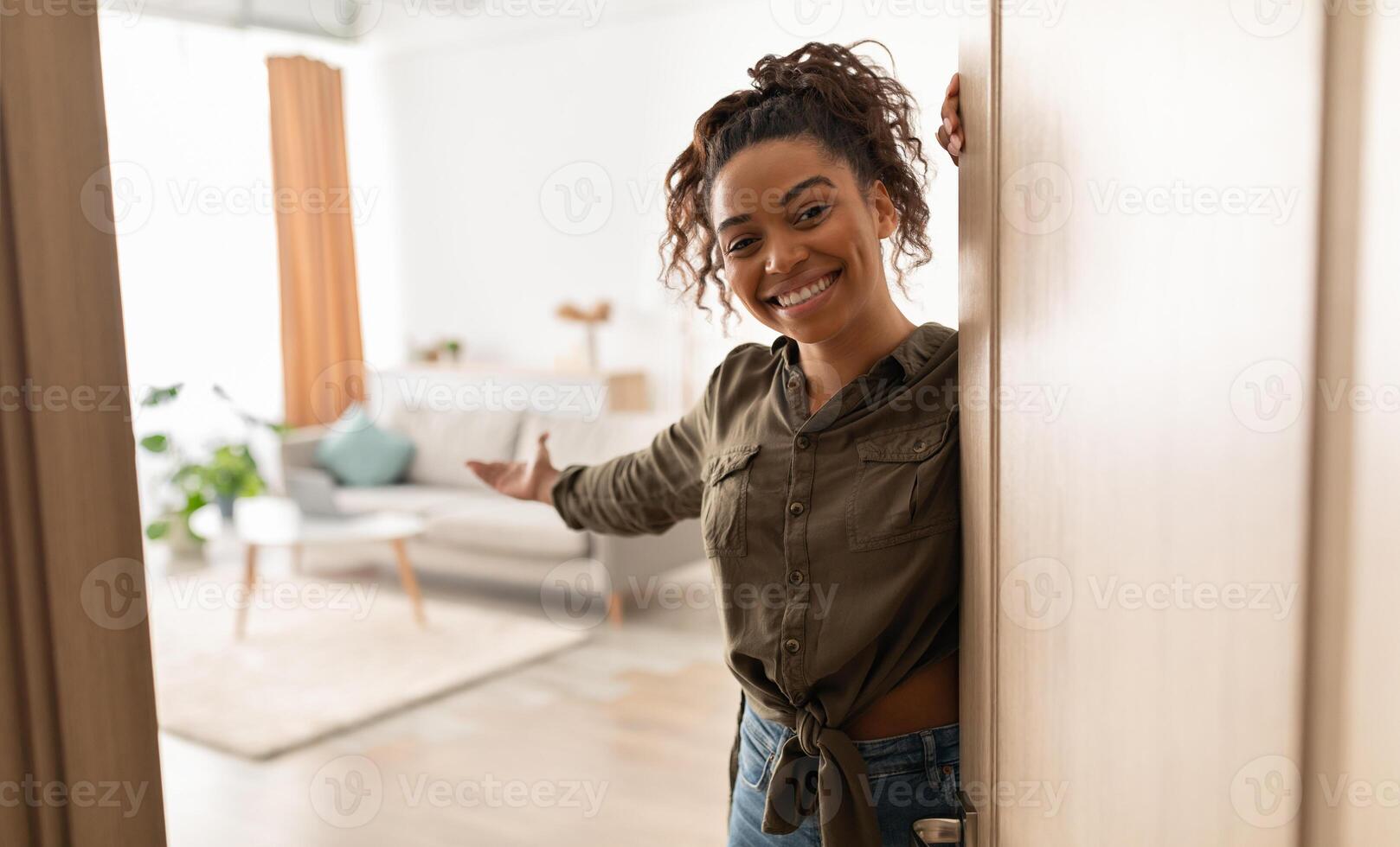 Welcome To My Home. Joyful Millennial Black Lady Opening Door And Gesturing Inviting To Come In Standing Indoors, Smiling To Camera. Real Estate Owner. Hospitality Concept photo