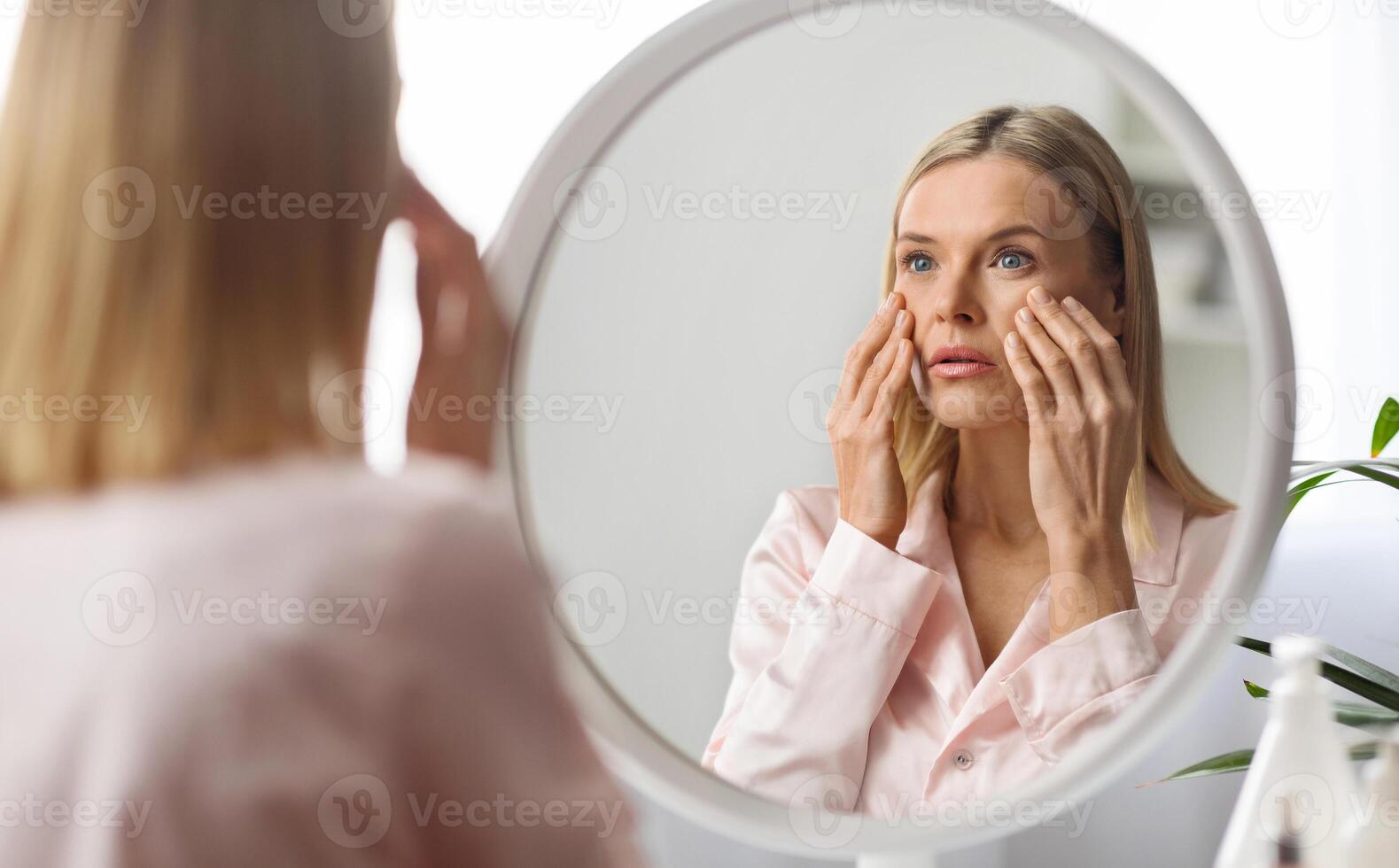 Skin Problems Concept. Upset Middle Aged Woman Looking At Mirror And Touching Face, Confused Mature Lady Noticed Wrinkles And Dark Circles Under Eyes, Unhappy With Skincare Routine, Selective Focus photo