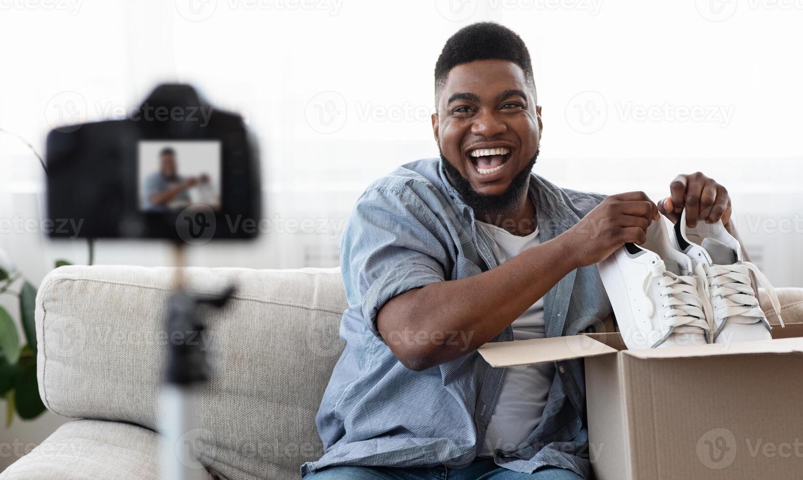 Joyful African American Man Blogger Recording Unboxing , Removing New Shoes Out Of Box At Camera, Free Space photo