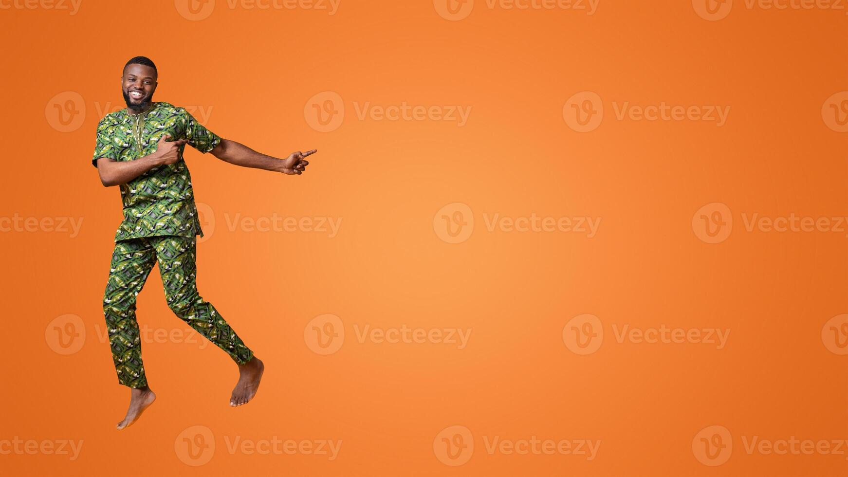 Excited black guy jumping up and pointing at free space, yellow studio background photo