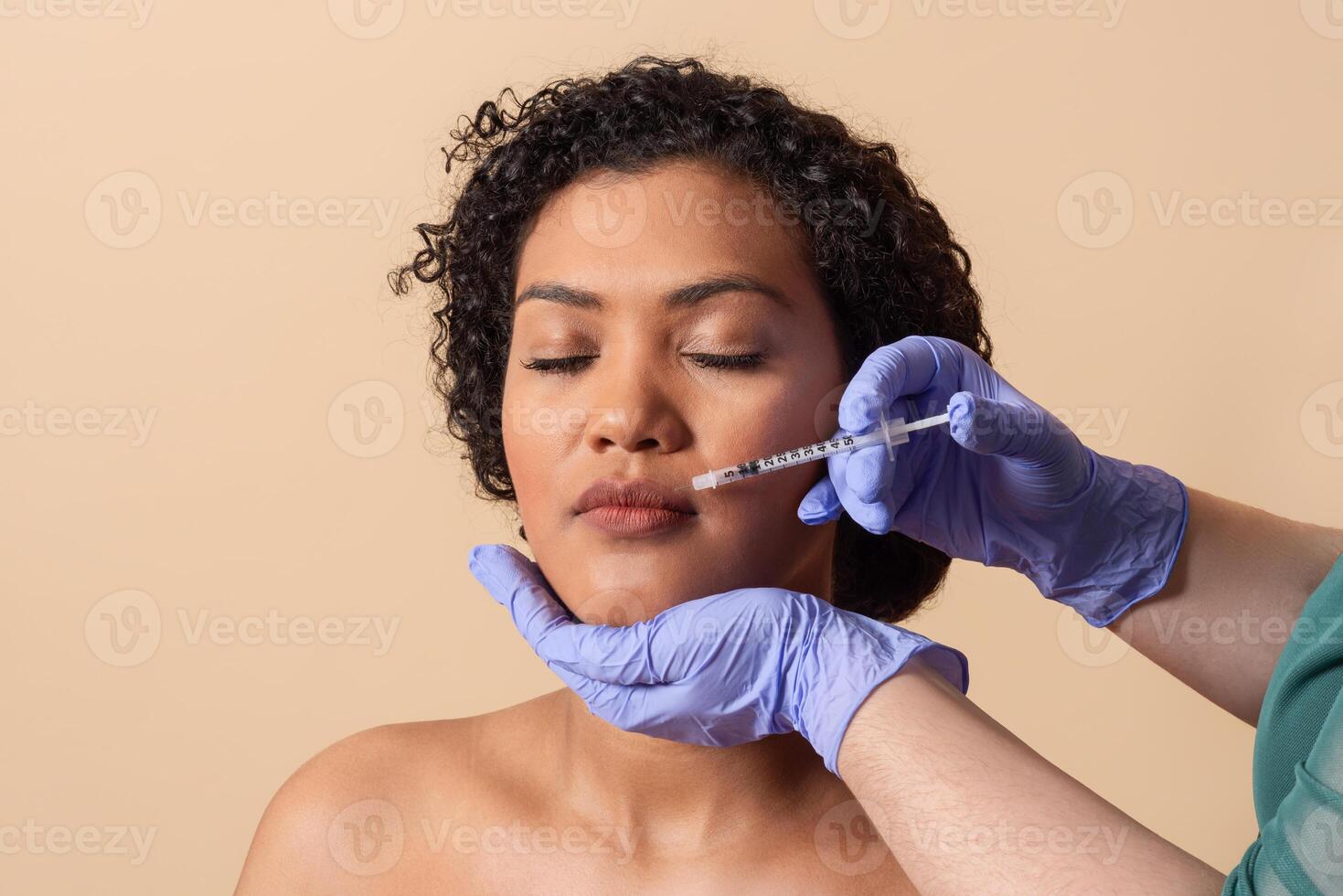 A woman with curly hair relaxes as a clinician administers injections to enhance her facial features in a well-lit medical office setting. The atmosphere feels calm and professional. photo