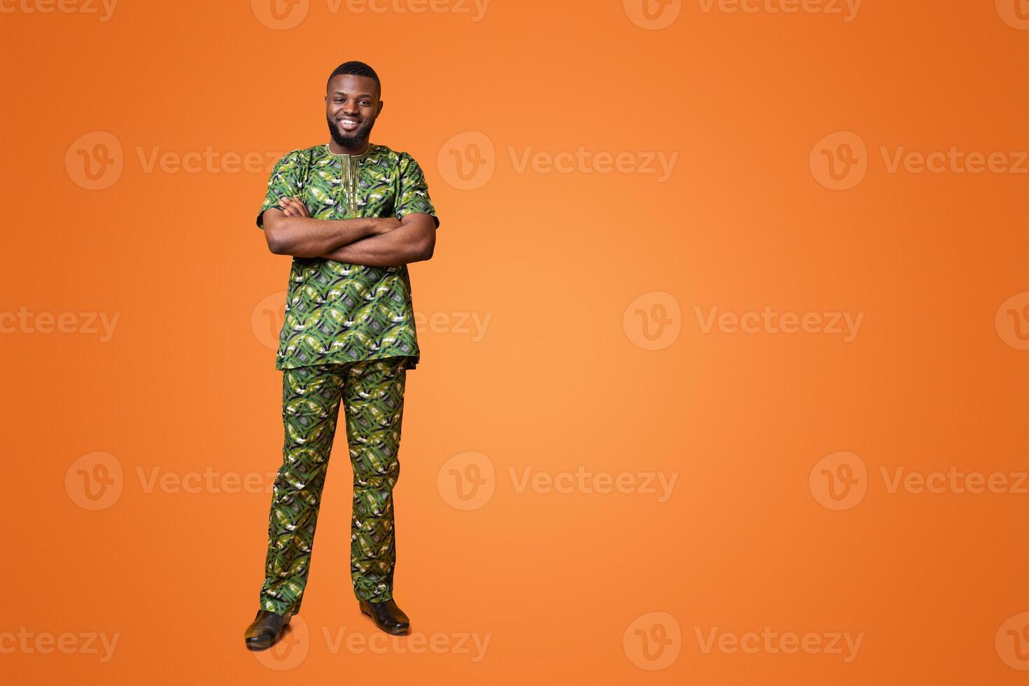 Smiling african american guy in authentic costume posing over yellow background, holding arms crossed photo