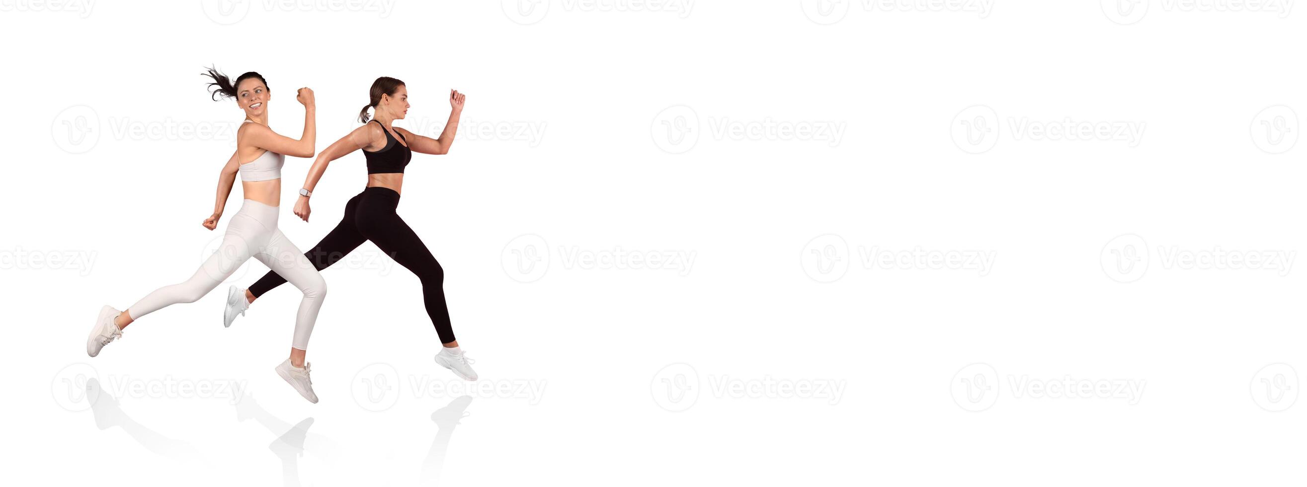 Two women are sprinting side by side in a modern fitness studio, showcasing their athleticism and teamwork. Their focused expressions emphasize dedication to health and exercise. photo
