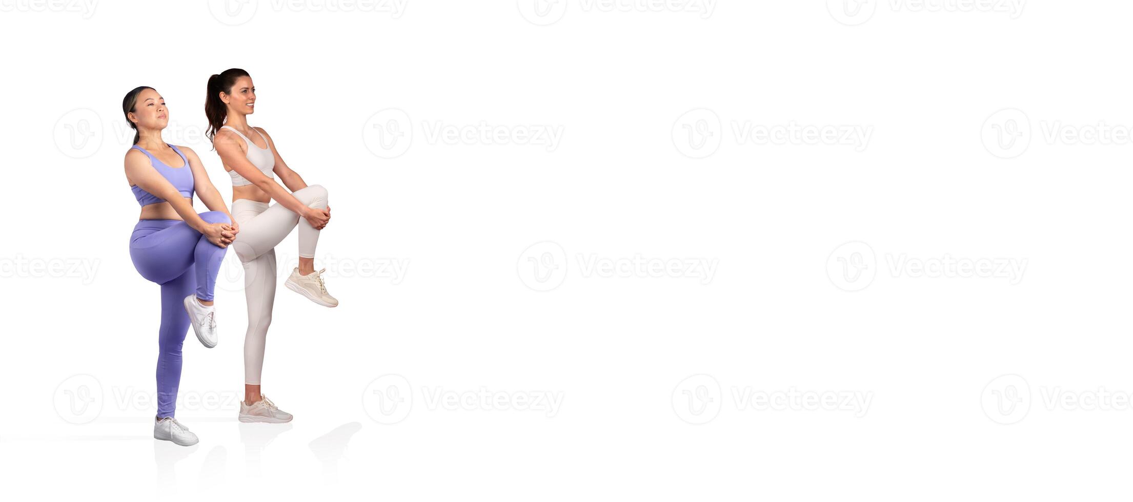Two women perform a workout routine indoors, focusing on leg raises while dressed in matching athletic outfits. The setting features a clean, minimalistic background. photo