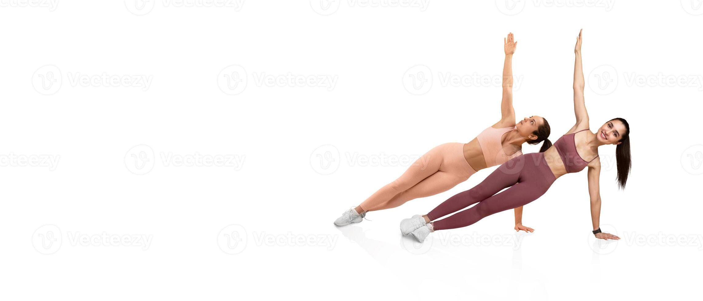 Two women in athletic clothing engage in a synchronized side plank exercise, showcasing their strength and fitness posture. The setting features a clean, minimalistic background. photo