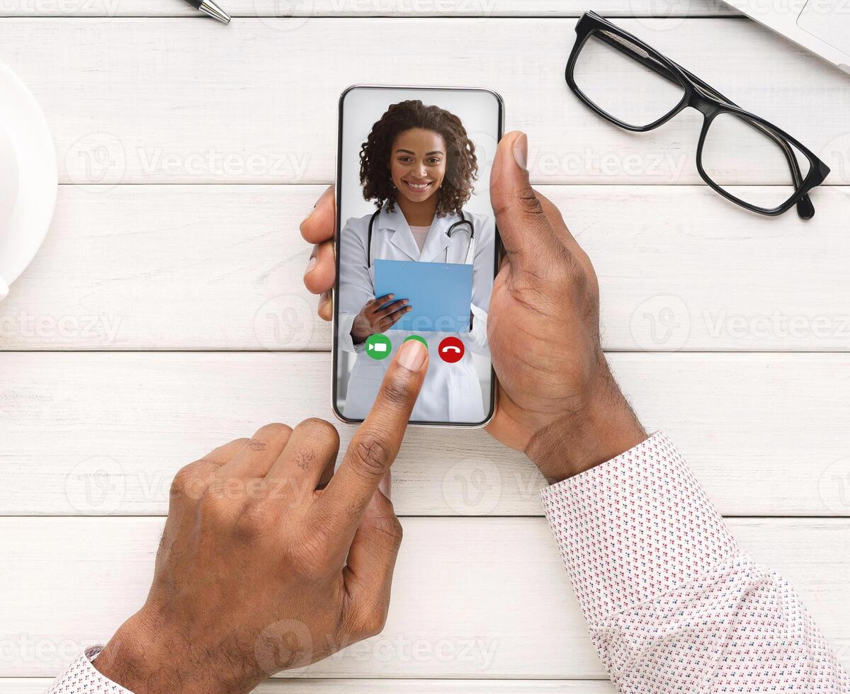 Unrecognizable Black Man Making Call To His Female Doctor While Working In Office, Having Web Conference With Smiling African Therapist Lady, Enjoying Telemedicine, Creative Collage, Top View photo