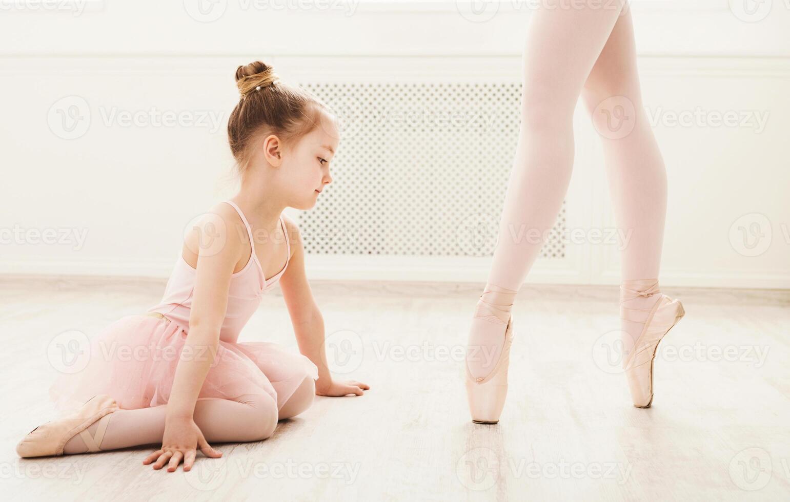 Little girl looking at professional ballet dancer. Cute baby dreaming to become ballerina, copy space. Classical dance school background, practicing for children, crop photo