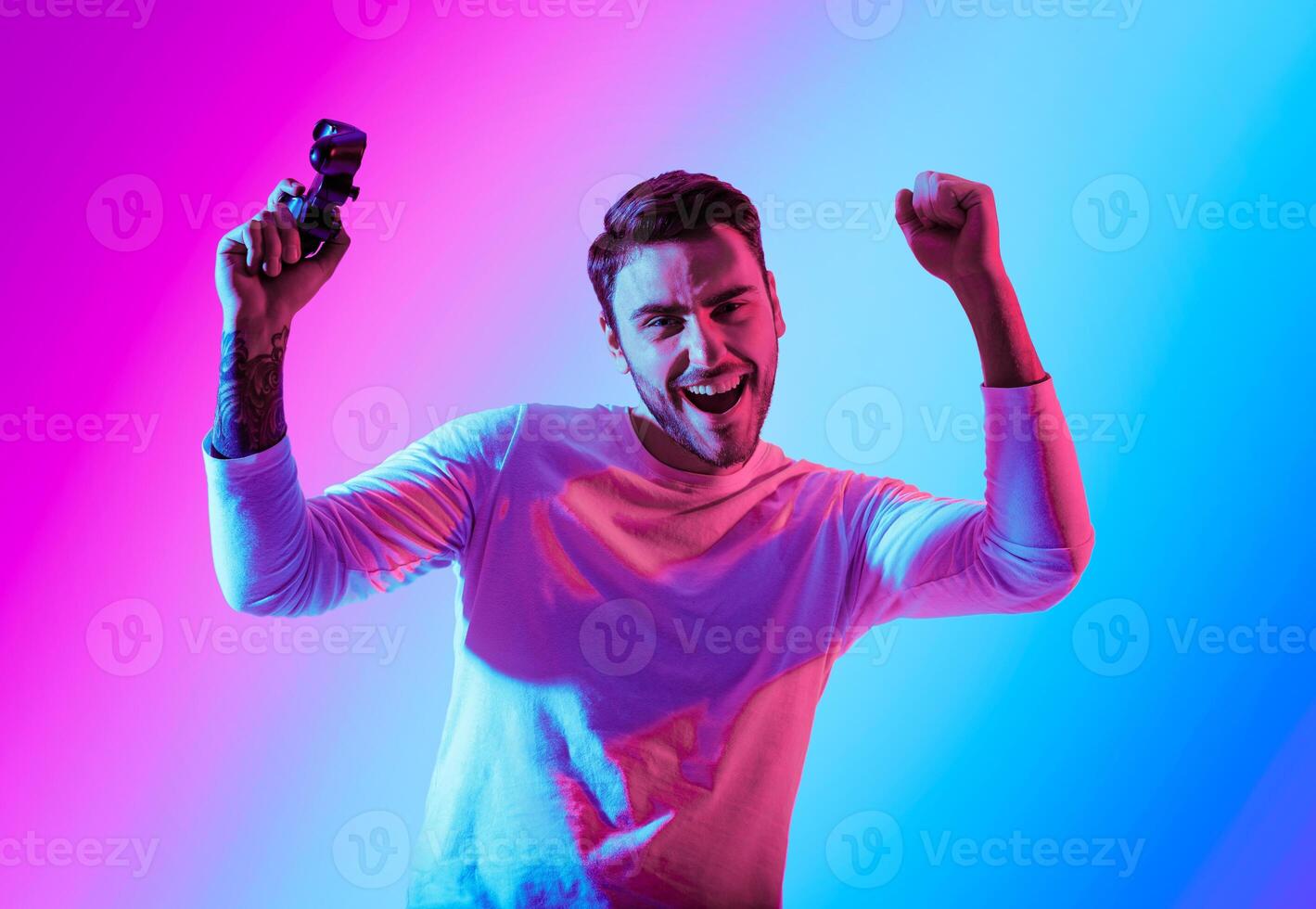Winning in computer game. Happy man raises hands with joystick, celebrating success, in neon, studio shot photo