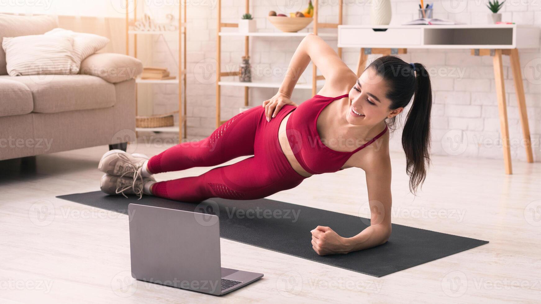 Coronavirus quarantine isolation. Active woman doing side plank while watching online sports tutorial at home photo
