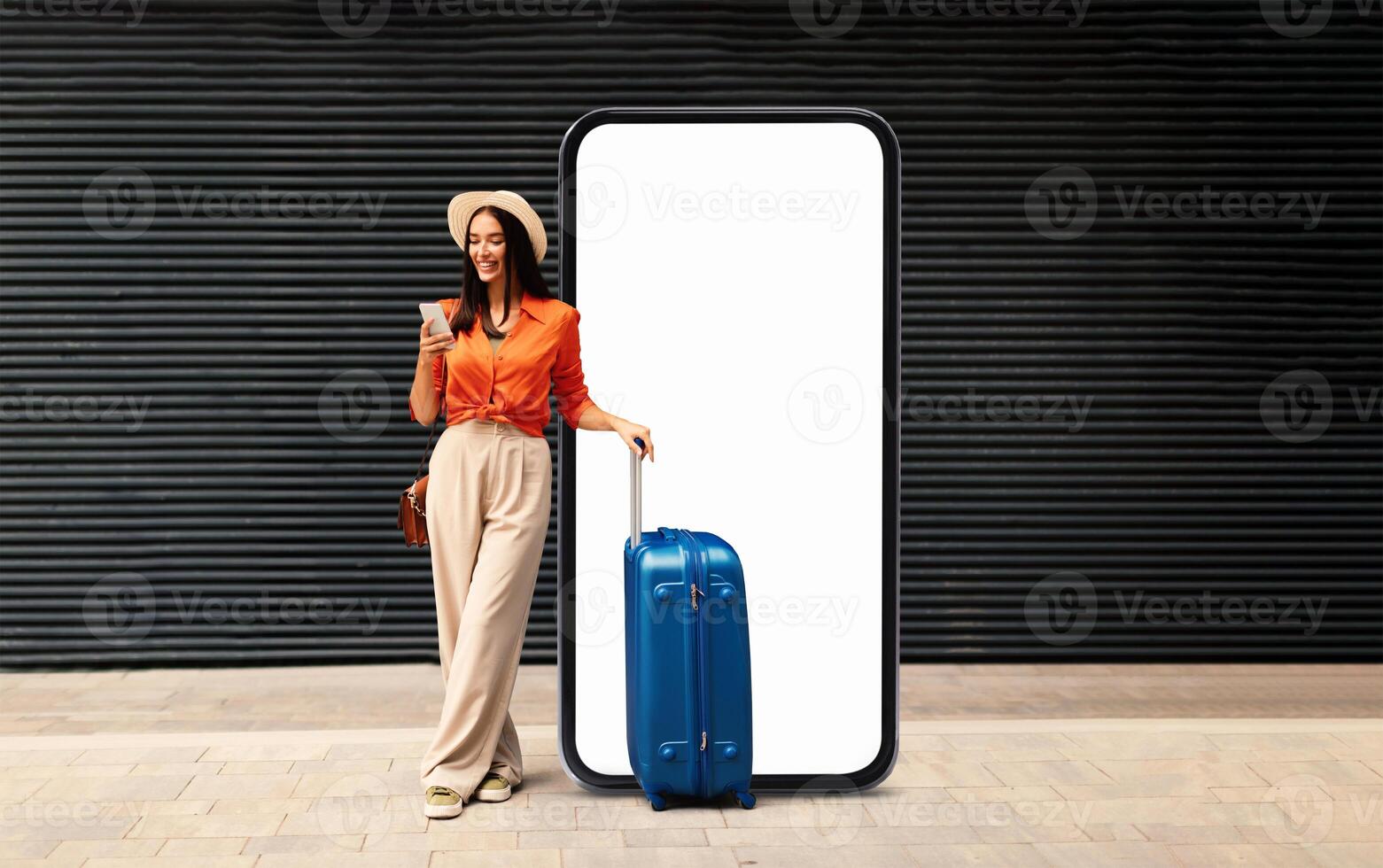 A woman stands confidently with a suitcase and coffee, wearing a fashionable outfit. She enjoys the outdoor atmosphere next to a large blank screen, perfect for ads or displays. photo