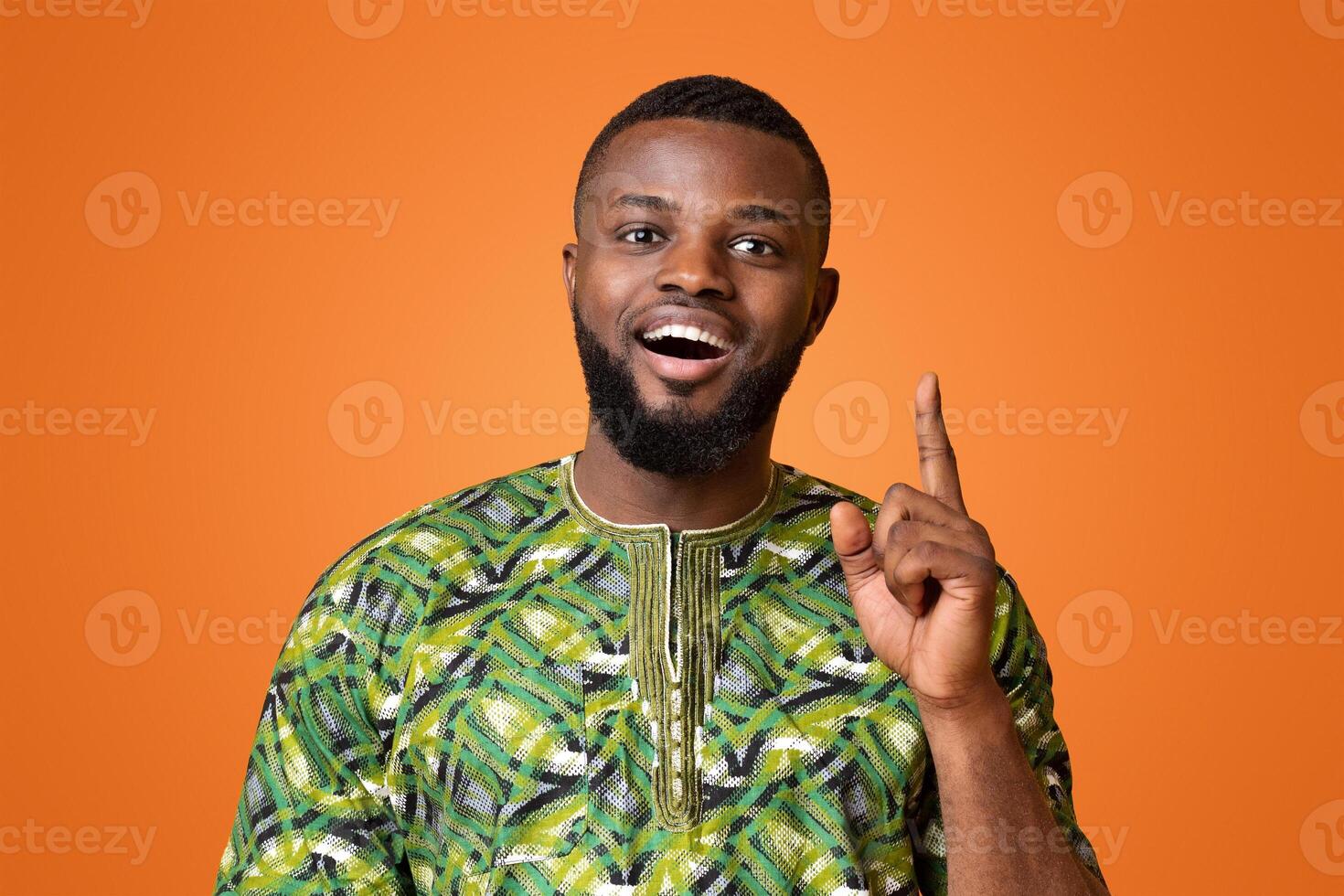 Inspired black man in traditional clothes having great idea, aiming finger up, yellow studio background photo
