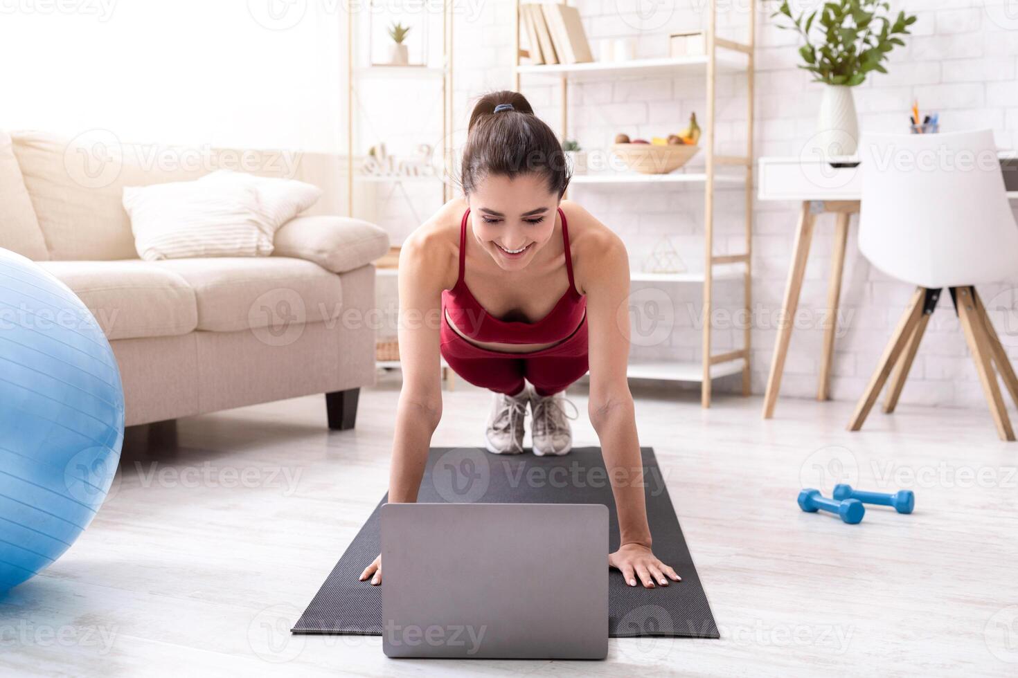 Active stay home pastimes. Millennial girl doing plank exercise to online tutorial indoors photo
