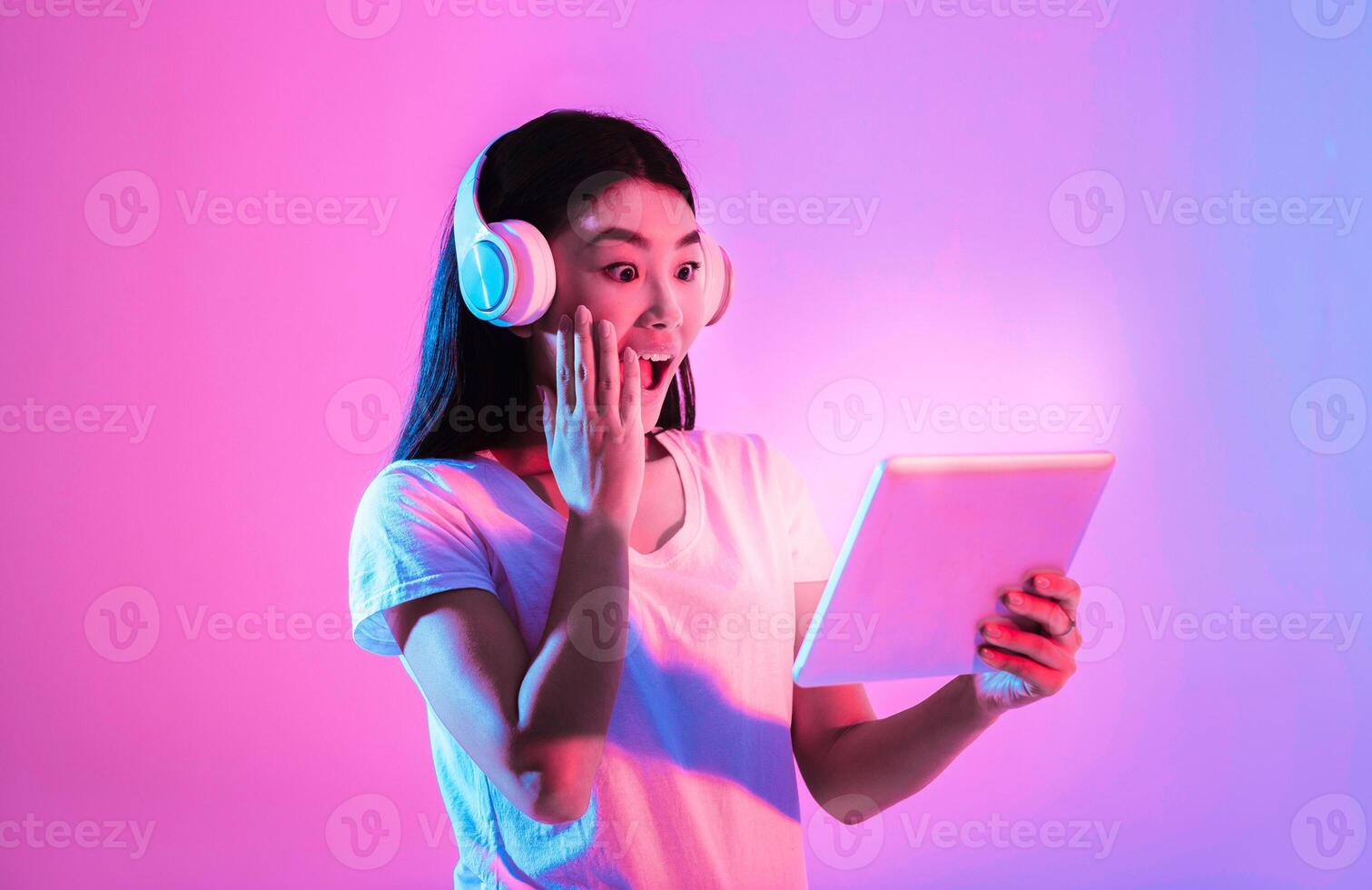 Surprised asian woman with tablet and wireless headphones, closed mouth with hand photo