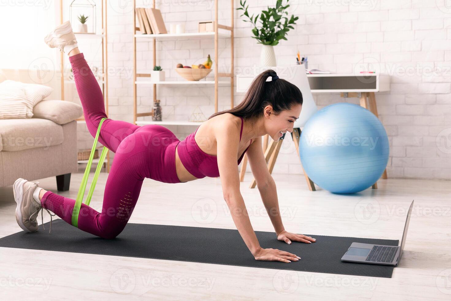 Stay home, stay fit. Happy girl working out with elastic band in front of laptop indoors photo