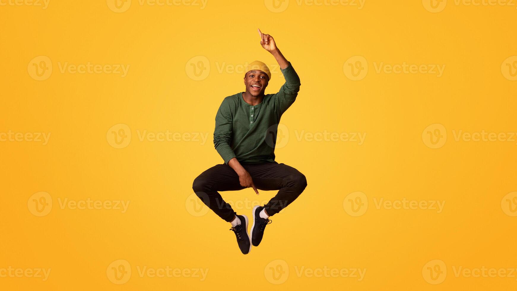 Check This. Cheerful Young Black Guy Pointing Up And Down While Jumping In Air, Positive Funny African American Hipster Man Demonstrating Free Copy Space On Yellow Background, Vertical Shot photo
