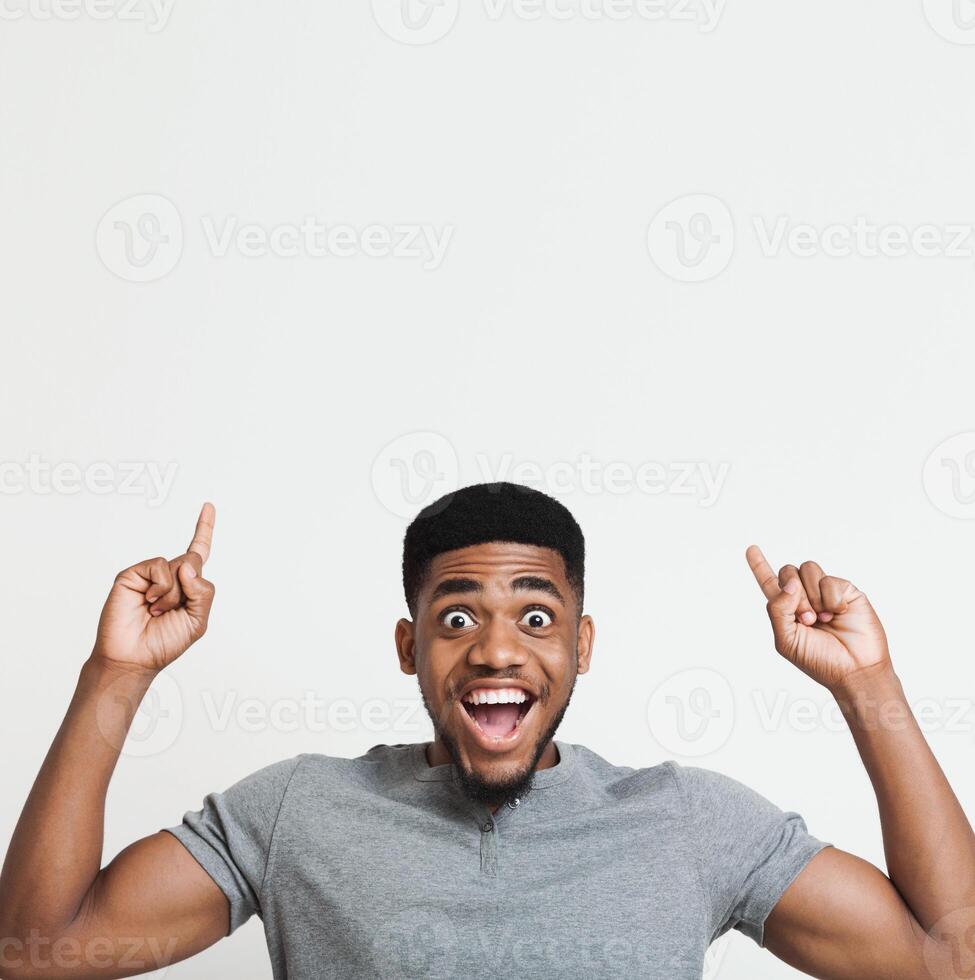 Excited african-american man having an idea and pointing two fingers up at copy space, white studio background photo