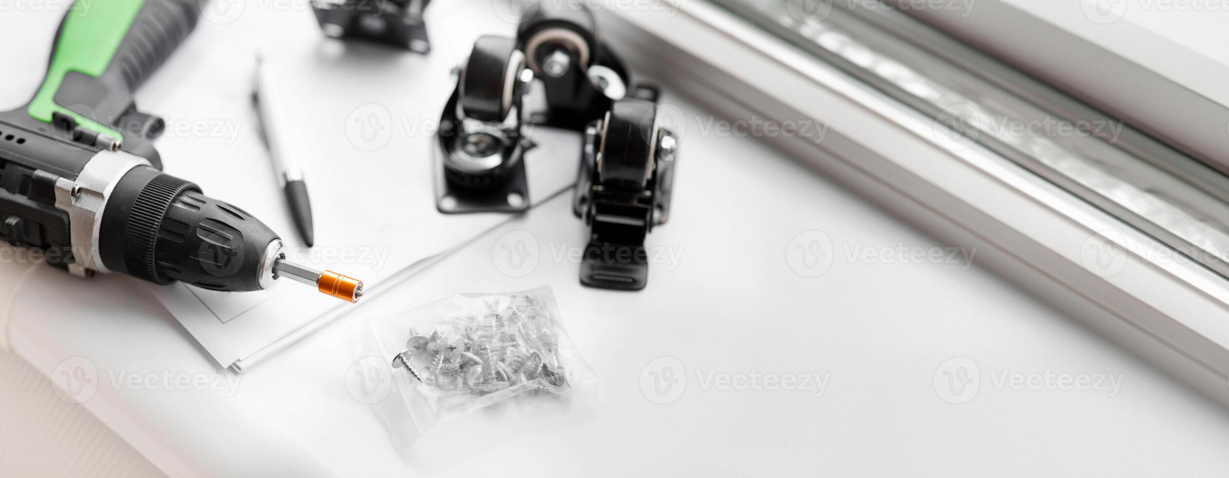 Collection tools for carpentry, furniture repair, renovation and assembly at home. Electric screwdriver, wheels and bolts and drilling on table, on white background, top view, close up, empty space photo