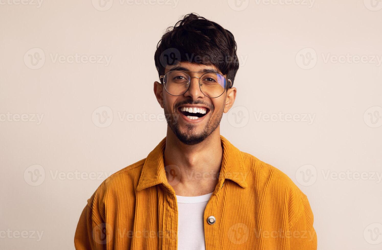 Closeup portrait of happy bearded arabic guy wearing glasses laughing at camera over grey studio background, copy space. Handsome middle-eastern young man in casual showing positive emotions photo