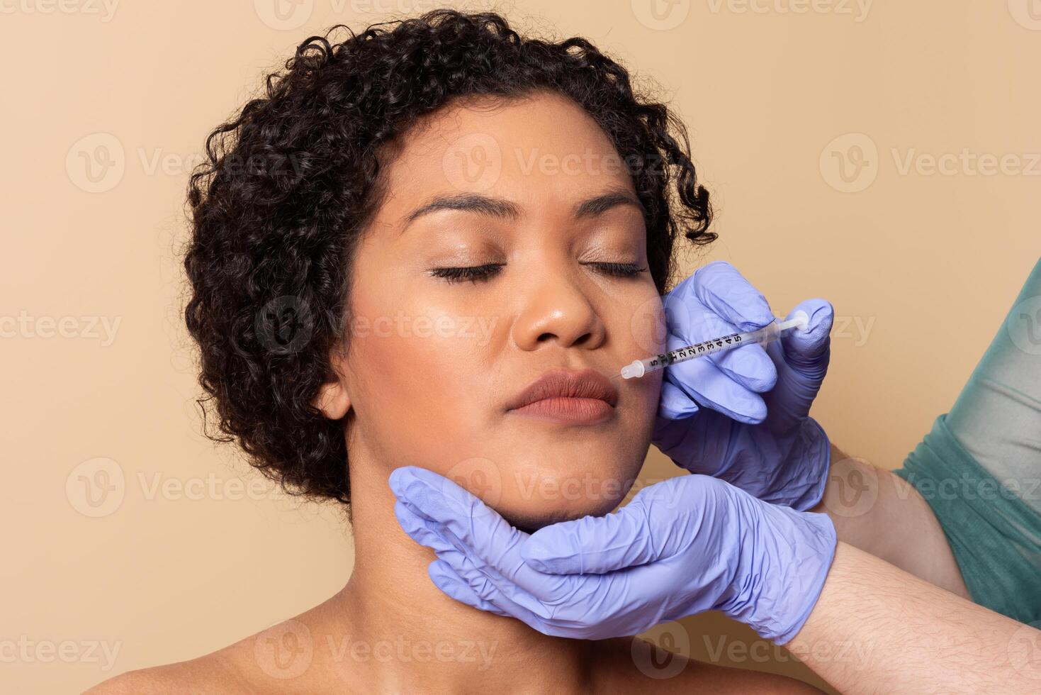 A woman with curly hair is receiving lip injections in a clinic. A professional wearing gloves carefully administers the treatment, ensuring the process is safe and effective. photo
