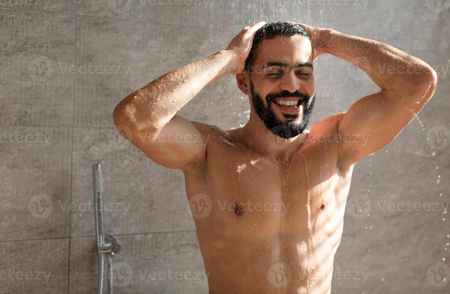 Portrait Of Happy Muscular Bearded Man Washing Hair And Body Using Male Shampoo Taking Hot Shower Standing Under Water Rain In Modern Bathroom At Home. Men's Beauty Routine And Hygiene Concept photo