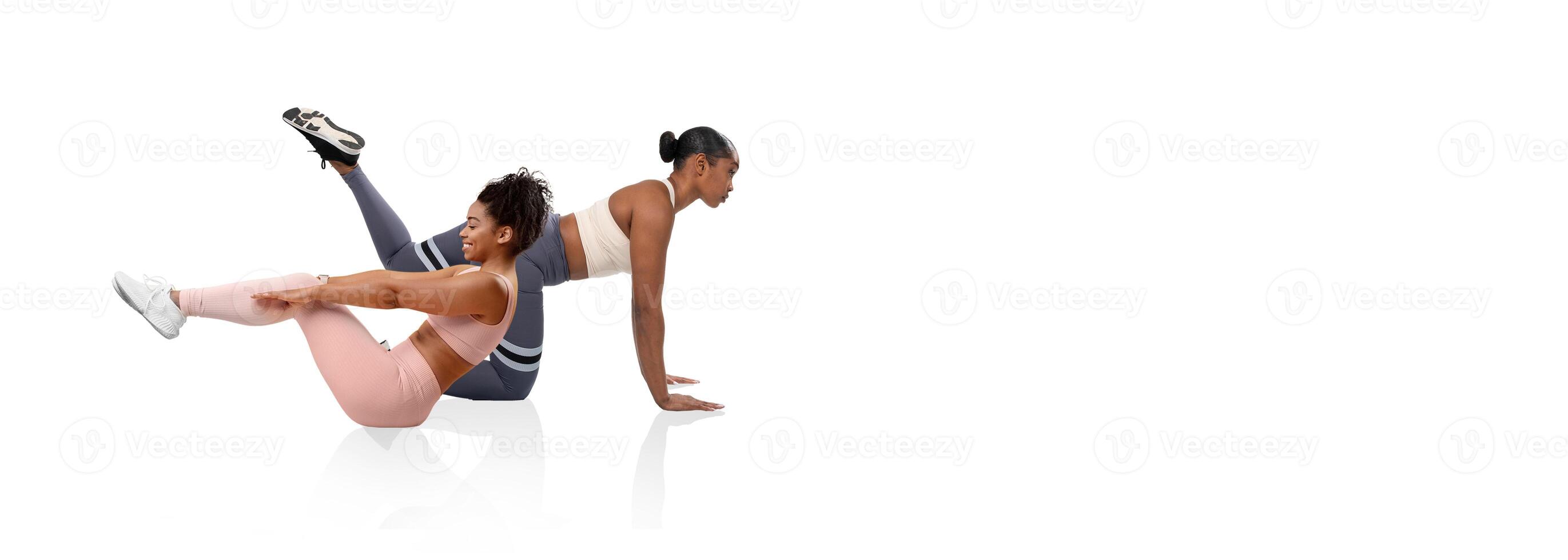 Two women perform a challenging workout routine in a fitness studio. One woman demonstrates a core exercise while the other focuses on maintaining her balance and strength. photo