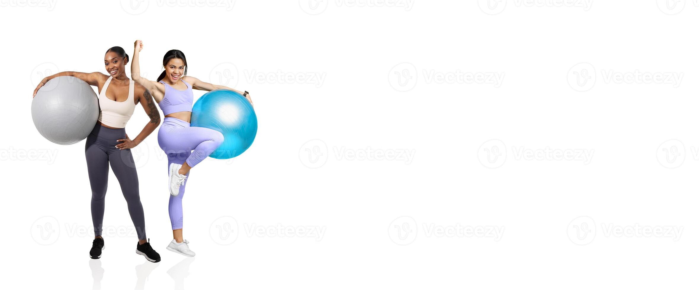 Two women smile while holding large exercise balls in a bright gym environment. They wear activewear and showcase a strong sense of fitness and camaraderie during their workout session. photo