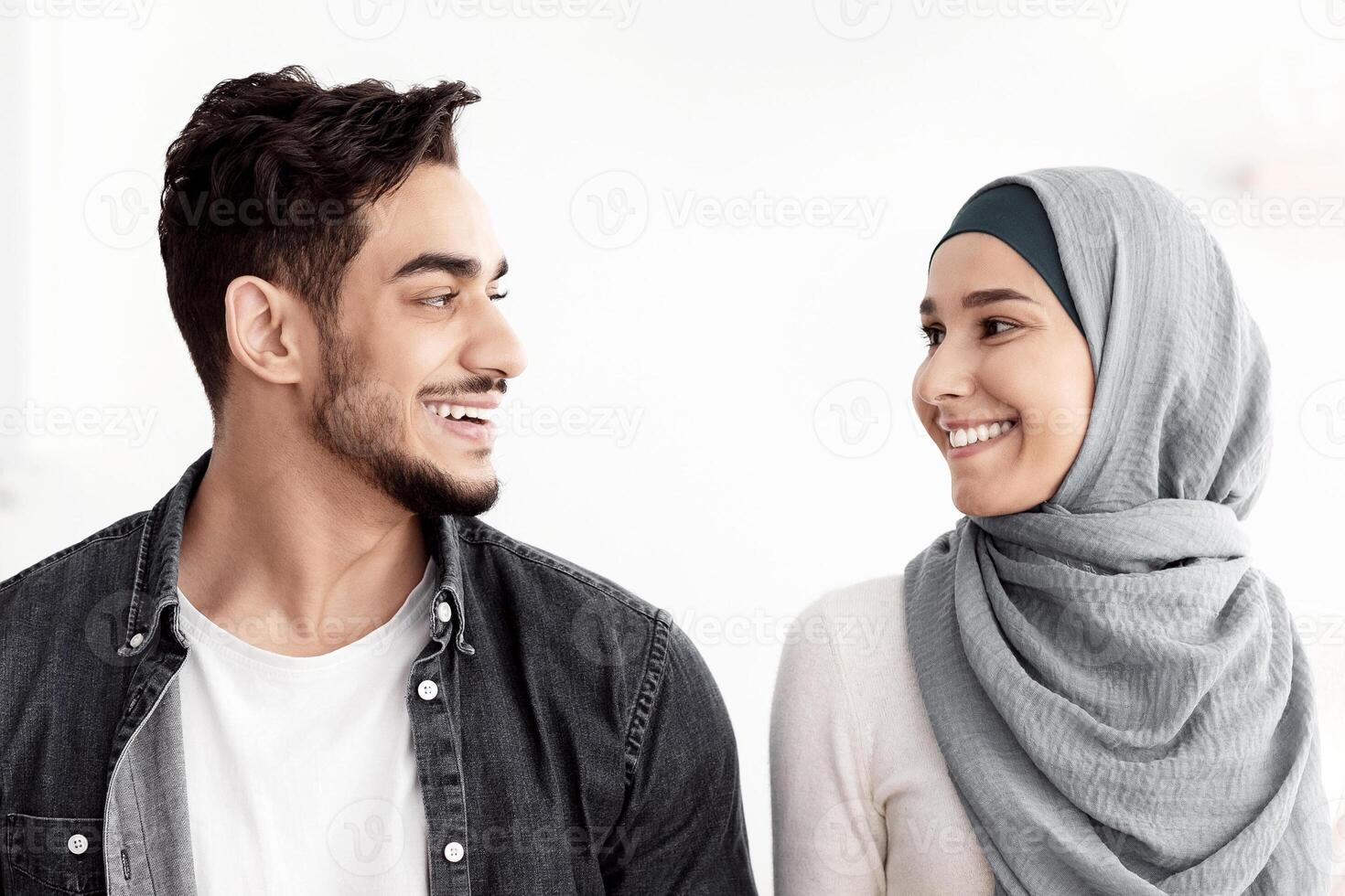 Happy muslim family cleaning their new apartment, holding house-keeping supplies and looking at each other in white kitchen, smiling, copy space. House-keeping, apartment cleaning concept photo