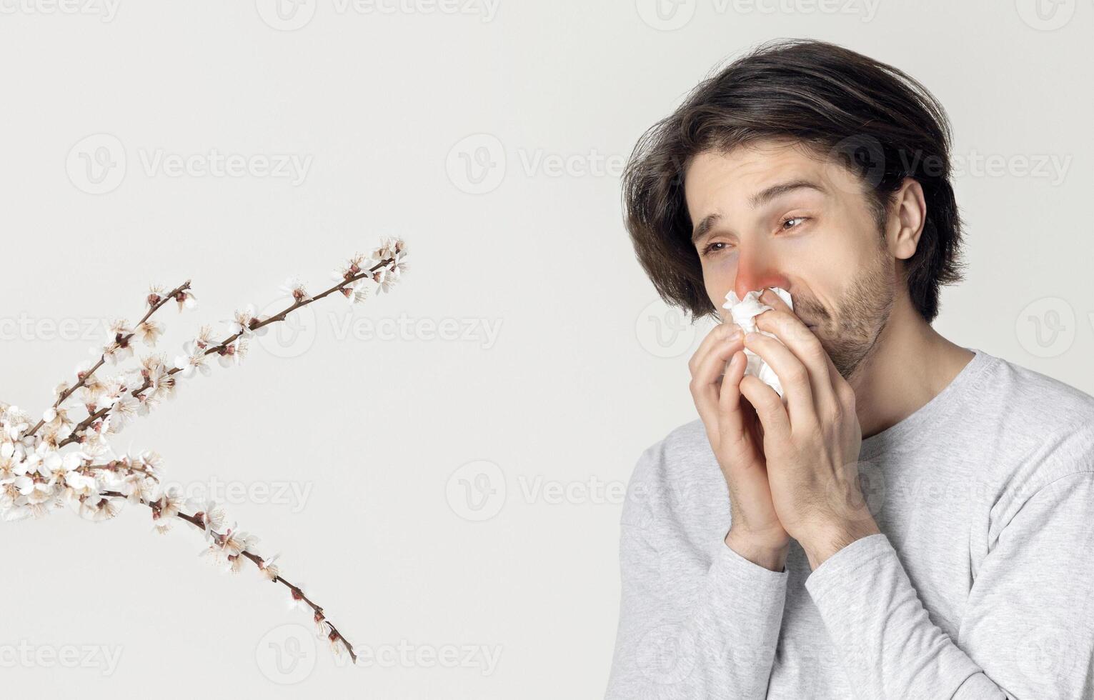 Man blowing nose near spring flowers. Pollen allergy symptoms photo
