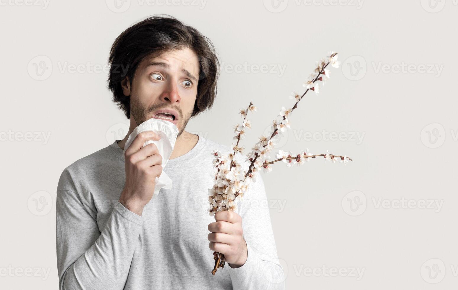 Fear of seasonal allergies. Man with napkin and red nose, looks at flowers photo