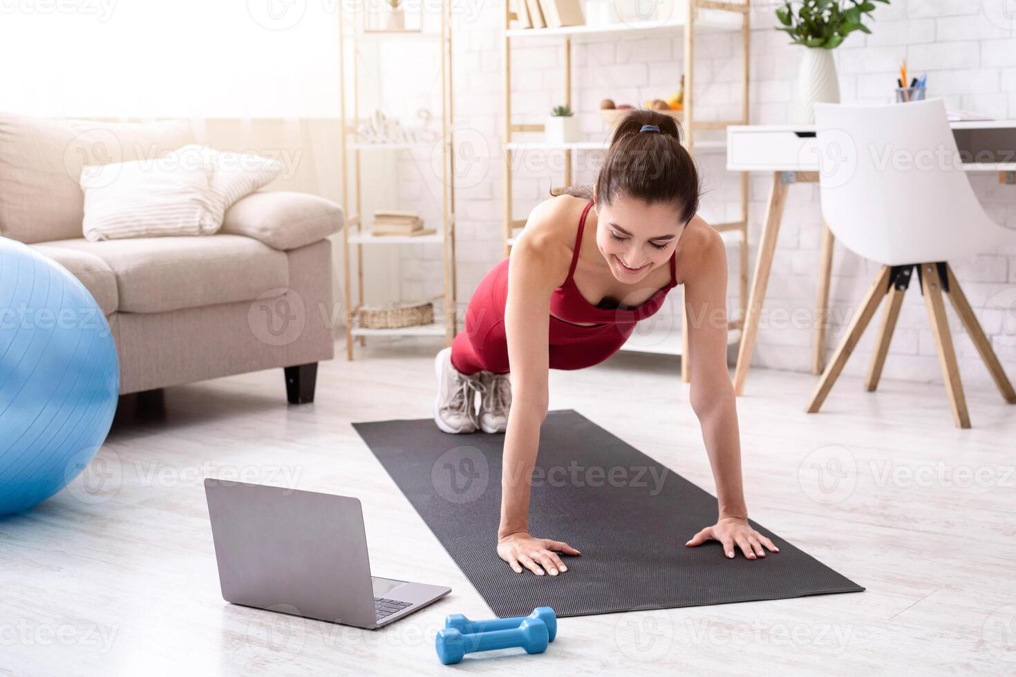 Personal trainer giving online workout class via laptop at home, doing plank or push up exercise photo