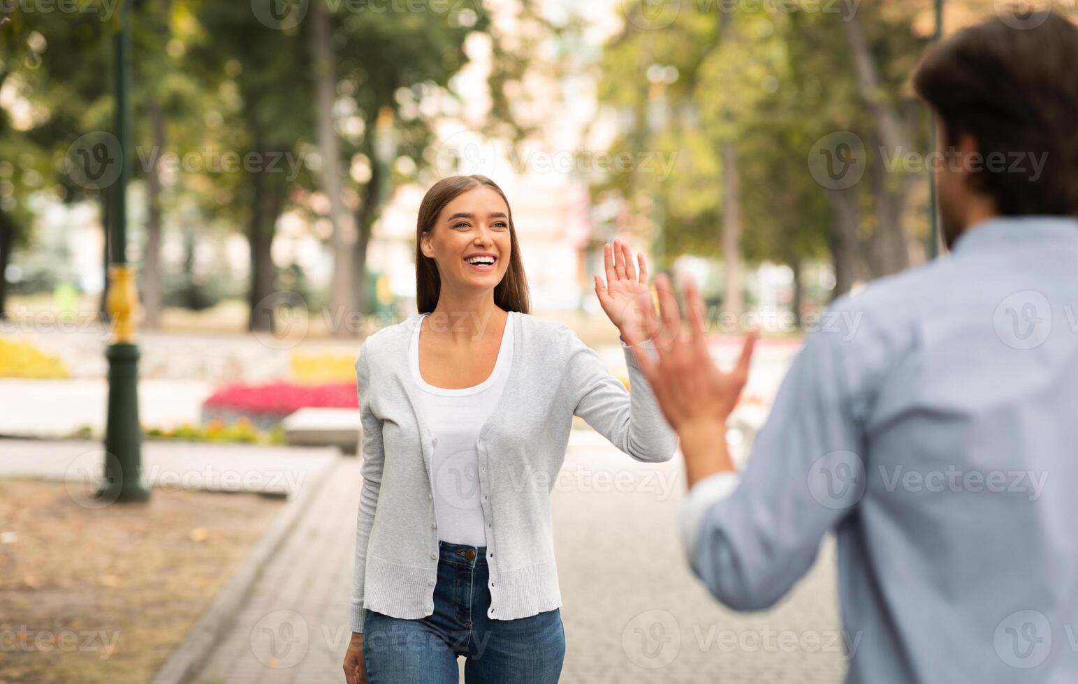 Just Friends. Girl Waving Hello Meeting Guy Walking In Park Outside. Selective Focus photo