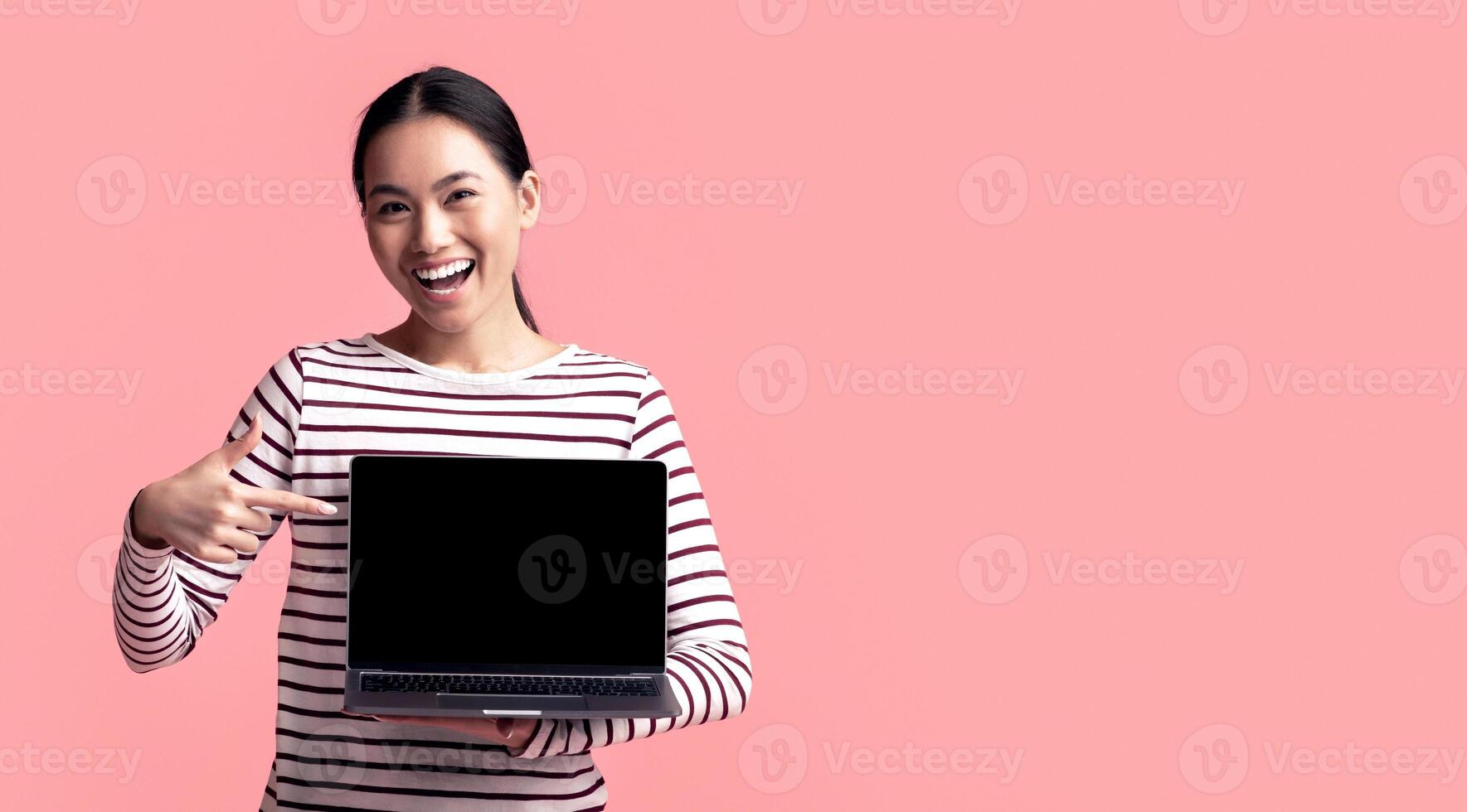 Happy Young Asian Woman Pointing At Laptop With Blank Black Screen In Her Hands, Excited Korean Lady Indicating Free Copy Space For Website Design, Standing Isolated On Pink Background, Mockup Image photo