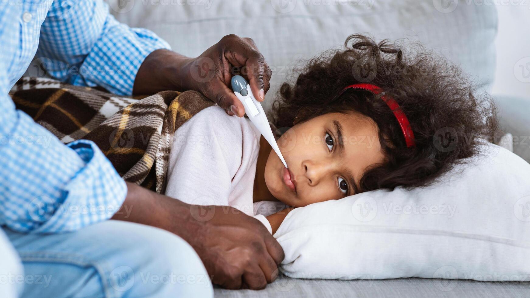 Infectious disease concept. Unhealthy African American child and her grandfather with thermometer at home photo