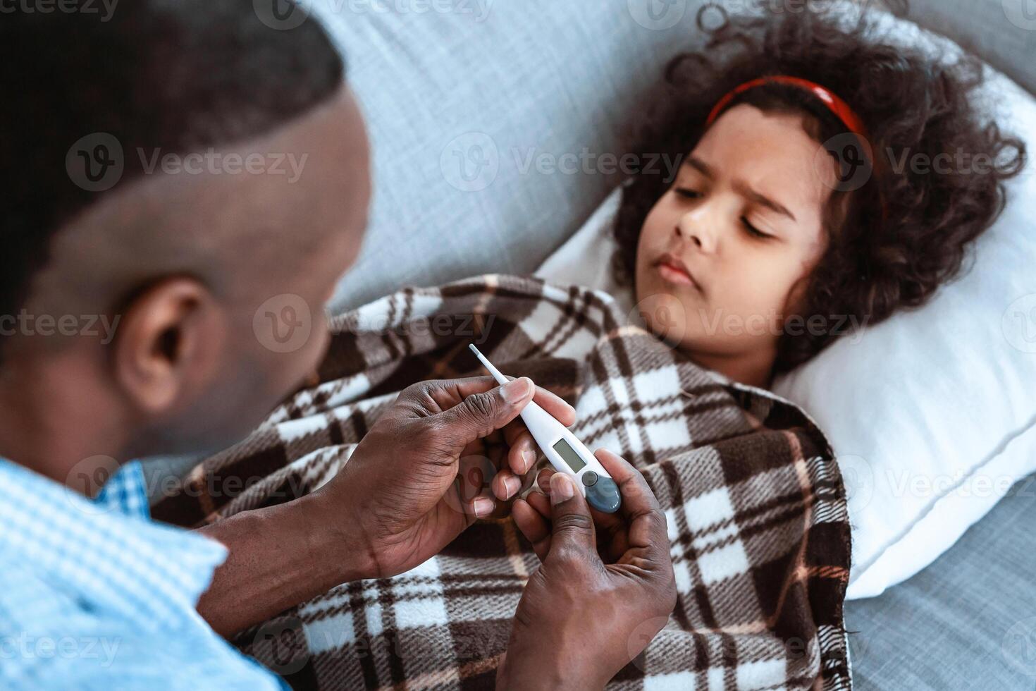 Coronavirus epidemic concept. Loving granddad with thermometer taking care of his sick granddaughter at home photo