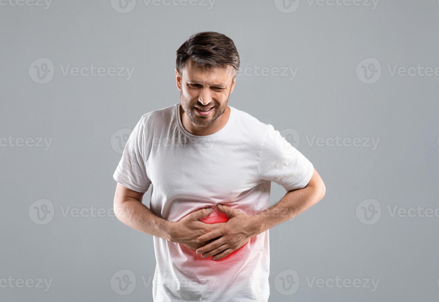 Middle-aged man holding his lightened with red right side, suffering from liver pain, grey studio background, copy space. Sad man having hepatitis, rubbing his right side. Liver diseases concept photo