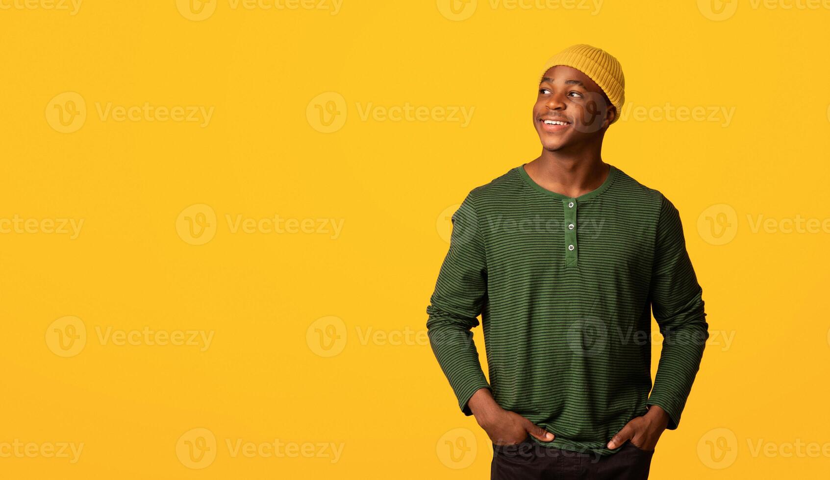 Nice Offer. Happy Millennial African American Guy Looking Aside At Copy Space, Cheerful Black Young Hipster Man In Orange Hat Standing With Hands In Pockets Over Yellow Background, Panorama photo