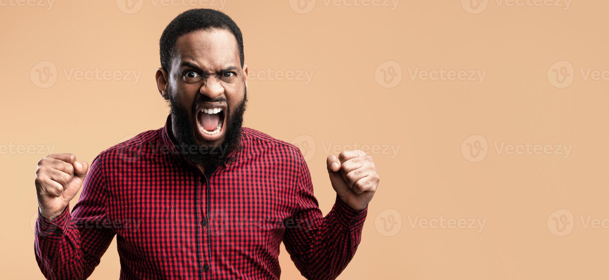 Human Emotions, Facial Expression Concept. Close up portrait of african man screaming with clenched fists, yellow studio photo