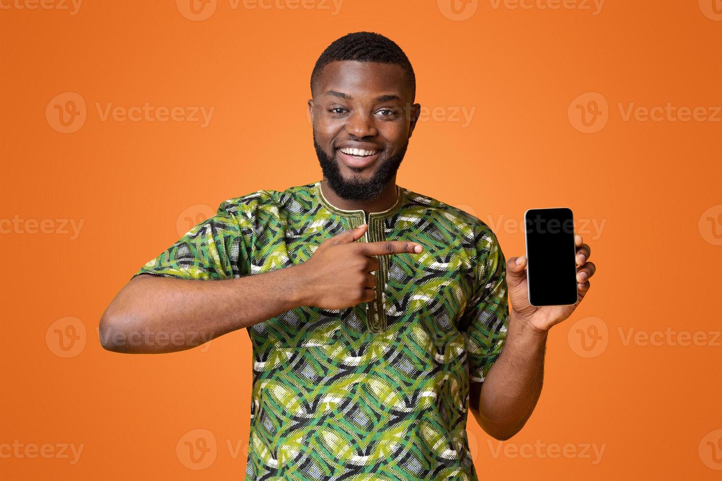 Happy african american man pointing at empty smartphone screen, recommending new application, yellow background photo