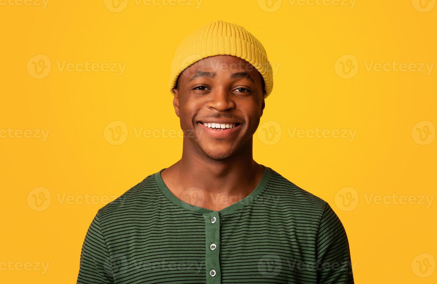Portrait Of Cheerful Young African American Guy In Orange Hat Smiling At Camera, Happy Millennial Male Having Fun While Posing Over Yellow Background In Studio, Closeup Shot With Free Space photo