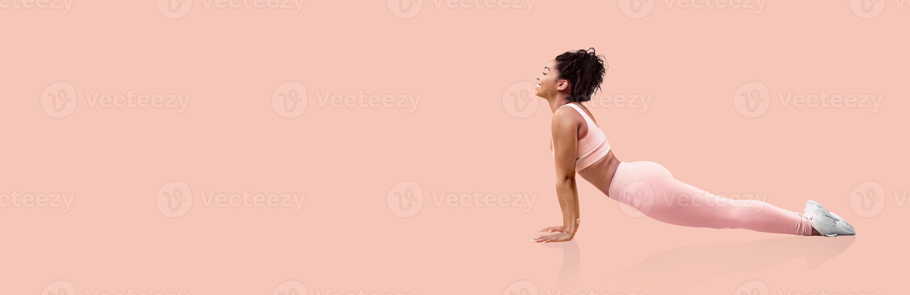 A woman performs a yoga pose in a minimalist pink studio. She focuses on her breath, engaged in a morning workout routine designed for flexibility and strength enhancement. photo