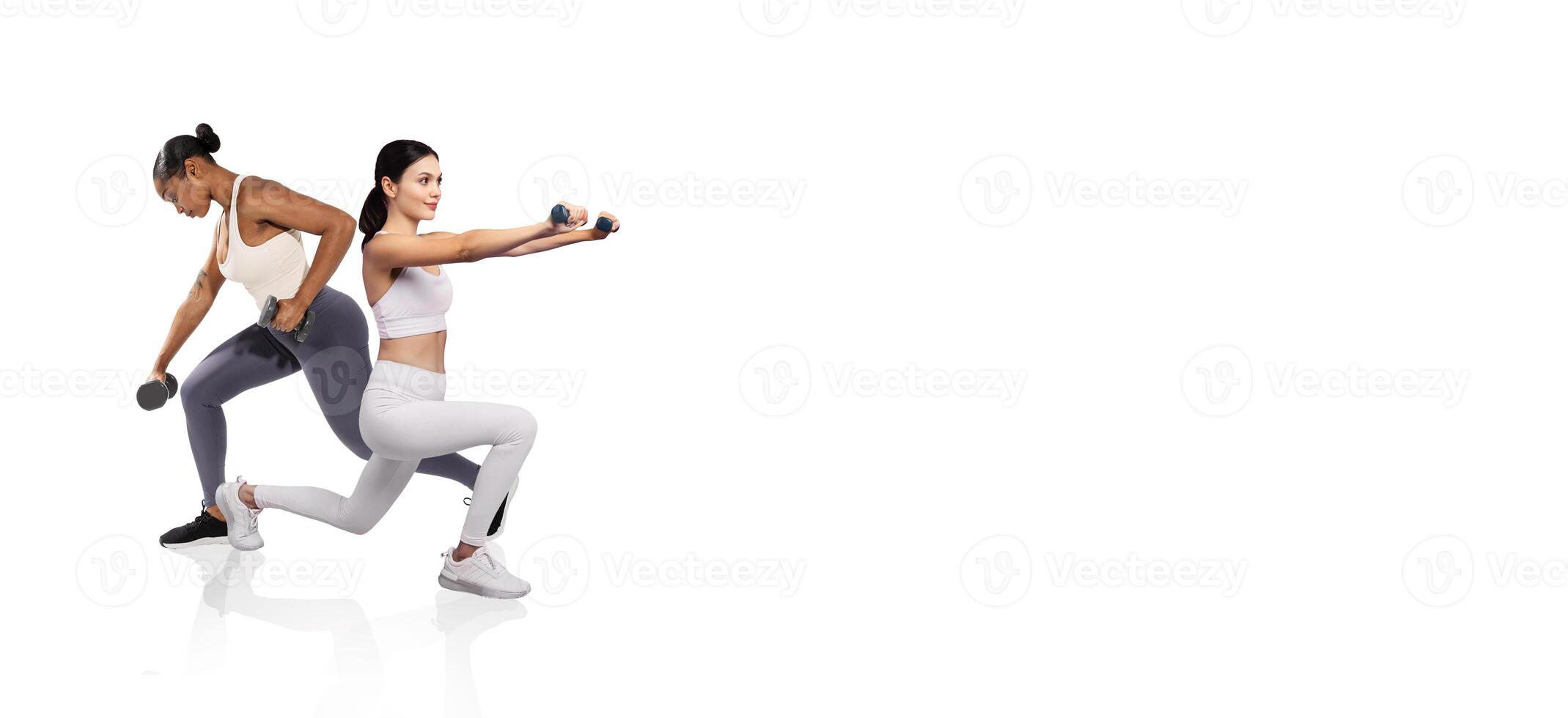 Two women are engaged in strength training exercises, each holding dumbbells. One is in a lunging position while the other completes a shoulder press. Bright lighting creates a motivated atmosphere. photo