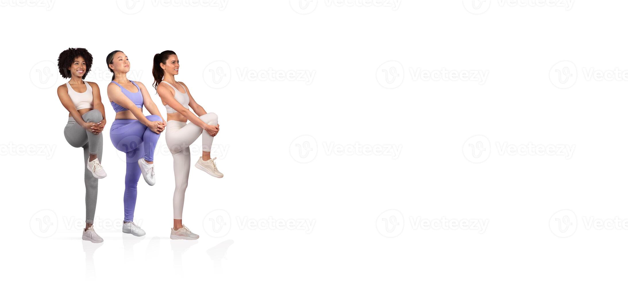 Three women in athletic wear are engaging in dynamic leg stretches, highlighting fitness and teamwork in a bright studio setting, promoting health and exercise awareness. photo