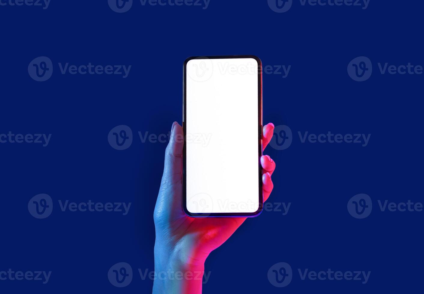 Smartphone in neon. Woman hand holds phone with empty screen isolated on blue background, close up, copy space photo