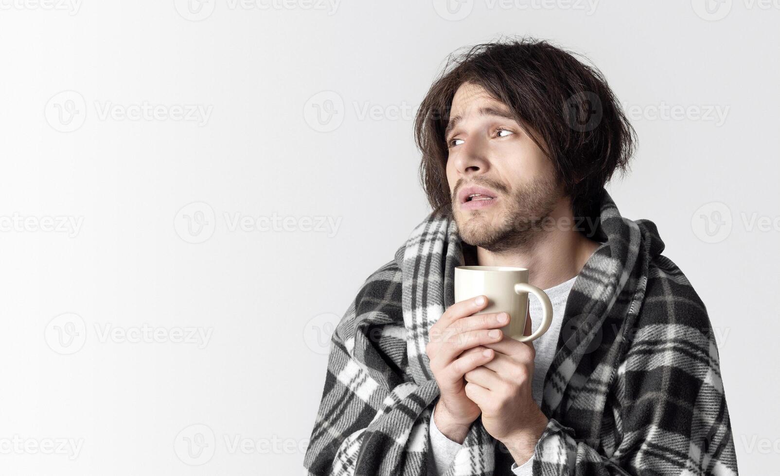 Sick exhausted man in plaid, holds cup of hot drink and looks at empty space photo