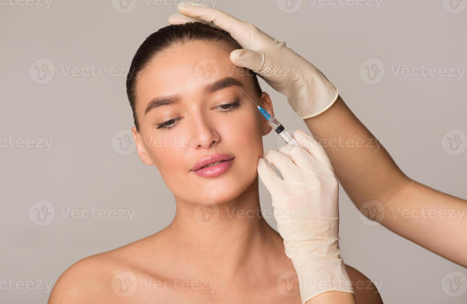 Plastic Surgery And Beauty Injection Concept. Young Woman Receiving Botox For Wrinkles, Isolated Over Studio Wall photo
