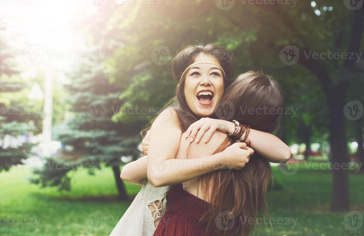 Two happy young girls hug each other. Females embracing, laughing and excited. Woman friendship, walk in the park outdoors. Asian boho girl with friend photo